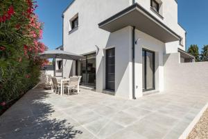 Cette maison blanche dispose d'une terrasse avec des chaises et un parasol. dans l'établissement Villa MOON - 600m plage - clim - 6 pers - Cap d'Agde, au Cap d'Agde