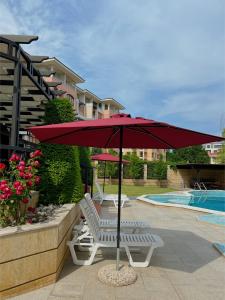un ombrellone rosso e due sedie bianche accanto a una piscina di Family Hotel Paradise a Sveti Konstantin i Elena