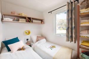 a small bedroom with two beds and a window at Camping Nature L'Airial in Soustons