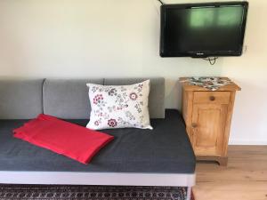 a couch with two pillows and a television on a wall at Ferienwohnung Morgentau am Rande der Wildnis in Sibratsgfäll