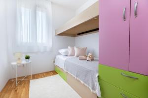 een kleine slaapkamer met een bed met roze en groene kasten bij Karlita Apartment in Solin