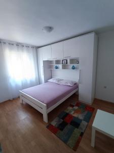 a white bedroom with a bed and a rug at Apartmani Biba in Novi Vinodolski