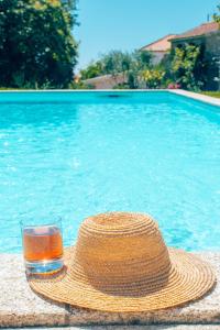 un sombrero de paja y una copa de bebida junto a la piscina en Just Like Home Casa do Castanheiro, en Afife
