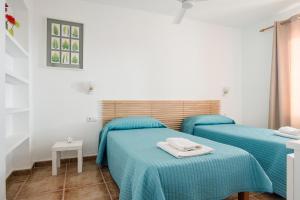 two beds in a white room with blue sheets at Apartamentos Mayans in Sant Ferran de Ses Roques