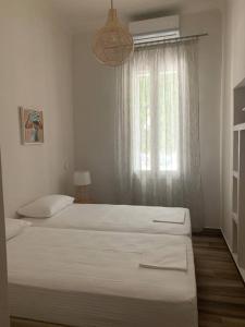 a white bedroom with two beds and a window at Alani house in Tinos