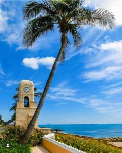 a clock tower with a palm tree next to the ocean at Wellington Garden in West Palm Beach