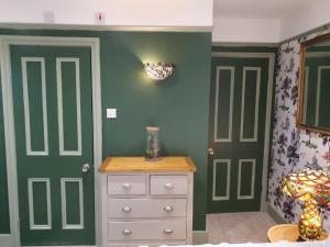 a bedroom with green walls and a white dresser and doors at The Lodge Stanwell in Stanwell