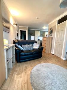 a living room with a black leather couch and a kitchen at Sandford House Apartment in Seaford