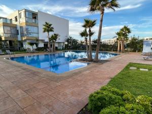 a swimming pool with palm trees and a building at Blue Beach, Sidi Rahal, Appartement pour familles in Sidi Rahal