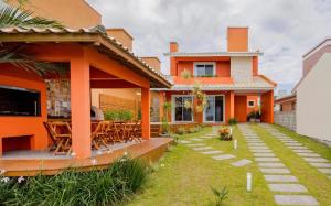 an orange house with a patio and lawn at Casa em Garopaba - Piscina - Forno para pizza - Ar condicionado - 3 quartos in Garopaba