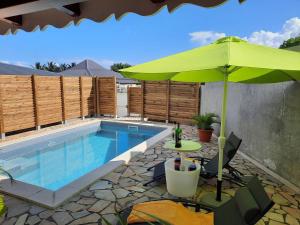 einem Pool mit einem grünen Sonnenschirm und einem Tisch mit in der Unterkunft bungalow hibis.kiss971 in Baie-Mahault