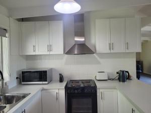 a kitchen with white cabinets and a stove and a microwave at Healesville Schofield Cottage in Healesville