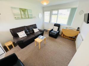 ein Wohnzimmer mit einem schwarzen Ledersofa und Stühlen in der Unterkunft 2 Bedroom Chalet SB113, Sandown Bay, Isle of Wight in Brading