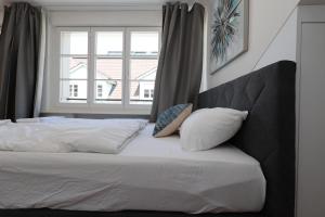 ein Bett mit weißer Bettwäsche und Kissen neben einem Fenster in der Unterkunft KoBi Apartments Falkenplatz in Luzern
