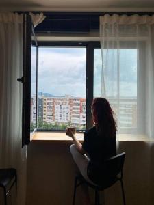une femme assise sur une chaise et regardant par une fenêtre dans l'établissement Sara blue apartment, à Tirana