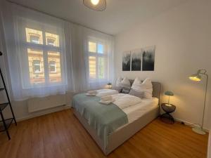 um quarto com uma cama com lençóis brancos e 2 janelas em LUCKY STAYS LS03 - 2 Zimmer - Luxus - Zentrum - große Küche - Aufzug - Smart-TV em Magdeburg