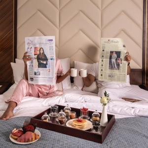 a person laying in bed reading newspapers with a tray of food at Jeddah Marriott Hotel Madinah Road in Jeddah