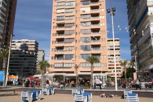 un edificio alto con sillas de playa enfrente en Apartamentos Don Vicente, en Benidorm