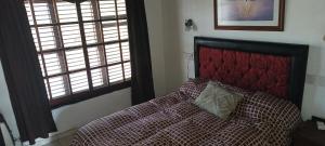 1 Schlafzimmer mit einem Bett mit einem roten Kopfteil und 2 Fenstern in der Unterkunft Casa con quincho y pileta in Cordoba
