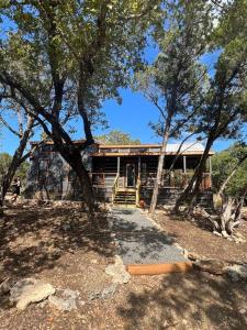 a log cabin with trees in front of it at Fox Hollow - Tiny home with Cypress Creek access, park like setting in Wimberley
