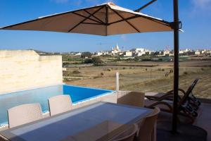 a table and chairs with an umbrella and a pool at Kenn Holiday Home in Għarb