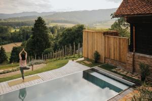 una mujer haciendo yoga en el borde de una piscina en Am Wildbachberg - Luxus Ferienhäuser mit Infinitypool, Privatsauna und Weinkeller, en Deutschlandsberg