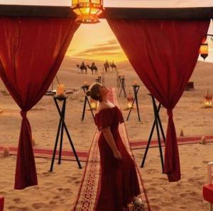 Uma mulher num vestido vermelho, parada no deserto. em Merzouga Top Luxury Camp em Merzouga