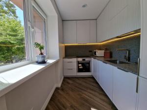a kitchen with white cabinets and a window at Oškinio Apartamentai in Palanga