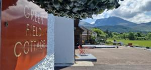 un cartel en un edificio con montañas en el fondo en Green Field Cottage at Ardenvale Self Catering en Fort William