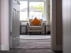 an orange pillow on a chair in a room with a window at 4 Bedrooms Homely House - Sleeps 6 Comfortably with 6 Double Beds,Glasgow, Free Street Parking, Business Travellers, Contractors, & Holiday-Goers, Near All Major Transport Links in Glasgow & City Centre in Glasgow