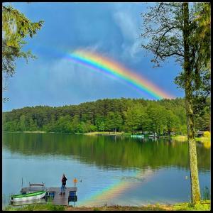 a rainbow over a lake with a person standing on a dock at Mazurska Sarenka in Wiartel