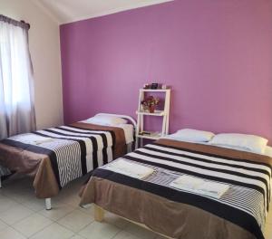 two beds in a room with a purple wall at Casa Lili in Oaxaca City