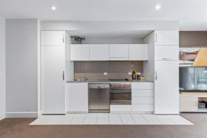Una cocina con gabinetes blancos y electrodomésticos de acero inoxidable. en Belle Escapes - Glenelg Shores Apartment, en Glenelg