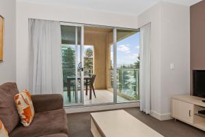 a living room with a couch and a television and a balcony at Belle Escapes - Glenelg Seaside Apartment in Glenelg