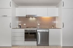 - une cuisine avec des placards blancs et un lave-vaisselle en acier inoxydable dans l'établissement Belle Escapes - Glenelg Seaside Apartment, à Glenelg