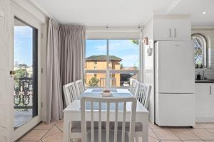 a white kitchen with a table and a refrigerator at Belle Escapes - Sunny Siesta at Glenelg in Glenelg