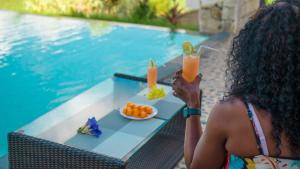 a woman holding up two drinks in front of a pool at JJ ET EUPHRASIE Lodge in Nosy Be