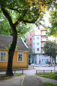 uma árvore sentada ao lado de um edifício amarelo ao lado de uma rua em BEST4YOU em Subotica