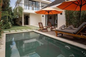 a pool with chairs and umbrellas next to a house at Echo Beach Duo in Canggu