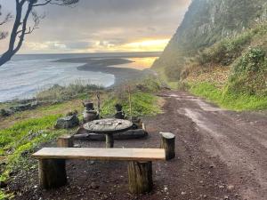 a bench on a dirt road next to the ocean at Kuanza Nature Experience, Fajã do Belo in Fajã da Caldeira de Santo Cristo