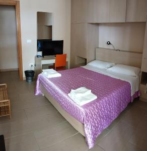 サン・フォカにあるHotel Blue Skyの紫色のベッド、デスク、テレビが備わるベッドルーム1室が備わります。