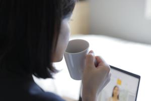 a woman holding a coffee cup in front of a computer at Super Hotel Tokyo Otsuka in Tokyo