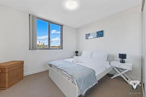 a white bedroom with a bed and a window at KozyGuru / Parramatta / APT / NPA008 in Sydney