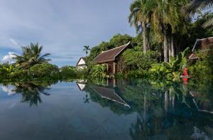 a pool of water with a house and palm trees at La Résidence Phou Vao, A Belmond Hotel, Luang Prabang in Luang Prabang