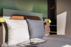 Una cama con almohadas blancas y un libro. en LyvInn Hotel Frankfurt Messe en Frankfurt