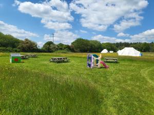 a playground in a field with picnic tables and tents at Dorset Glamping Fields in Corfe Mullen