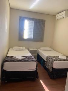 Duas camas num pequeno quarto com uma janela em Flor Que Ri - Flats Mobiliados na Melhor Localização em Olímpia