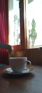 a cup on a plate on a table with a window at Chandan Guest House in Leh