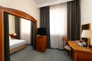 ブダペストにあるDanubius Hotel Hungaria City Centerのベッド、デスク、テレビが備わるホテルルームです。