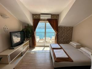 1 dormitorio con 1 cama, TV y balcón en Apartments Sun House, en Herceg-Novi